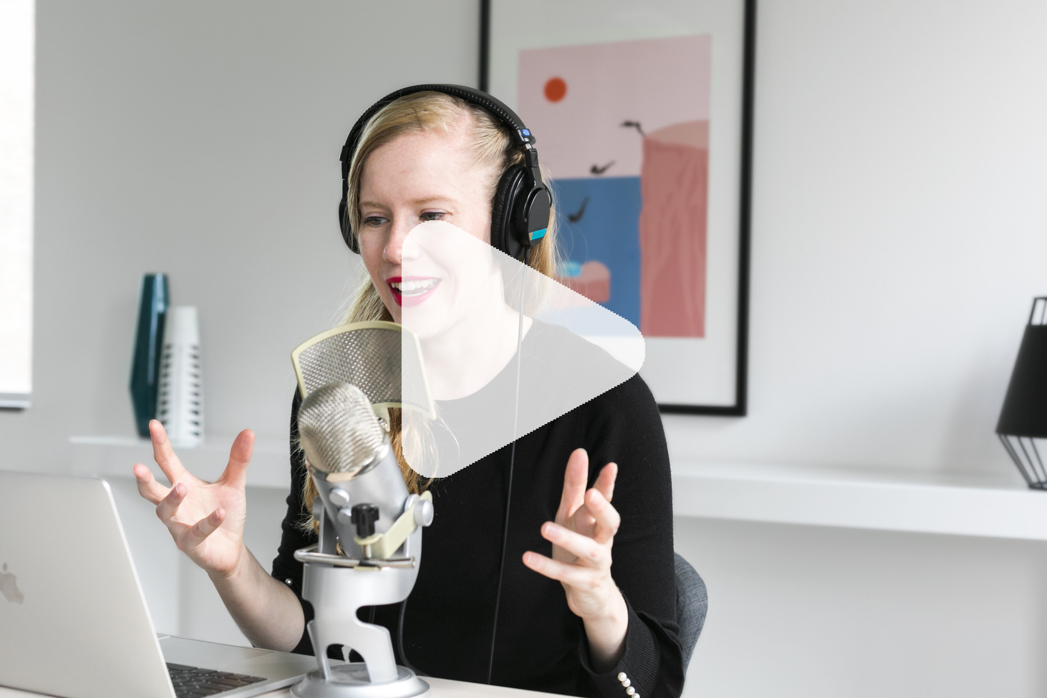 A woman sits at a microphone, reading from a laptop screen.