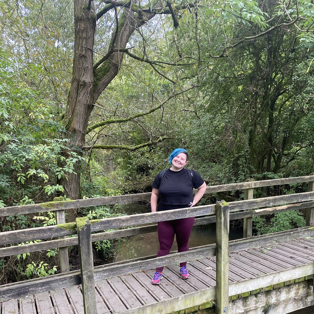A photo of Sarah standing on a wooden bridge in a forest